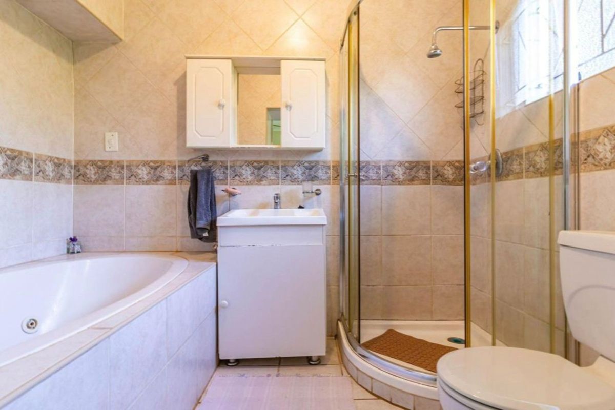 A functional bathroom featuring a built-in bathtub, corner shower enclosure, vanity cabinet with storage, and neutral ceramic wall and floor tiling.