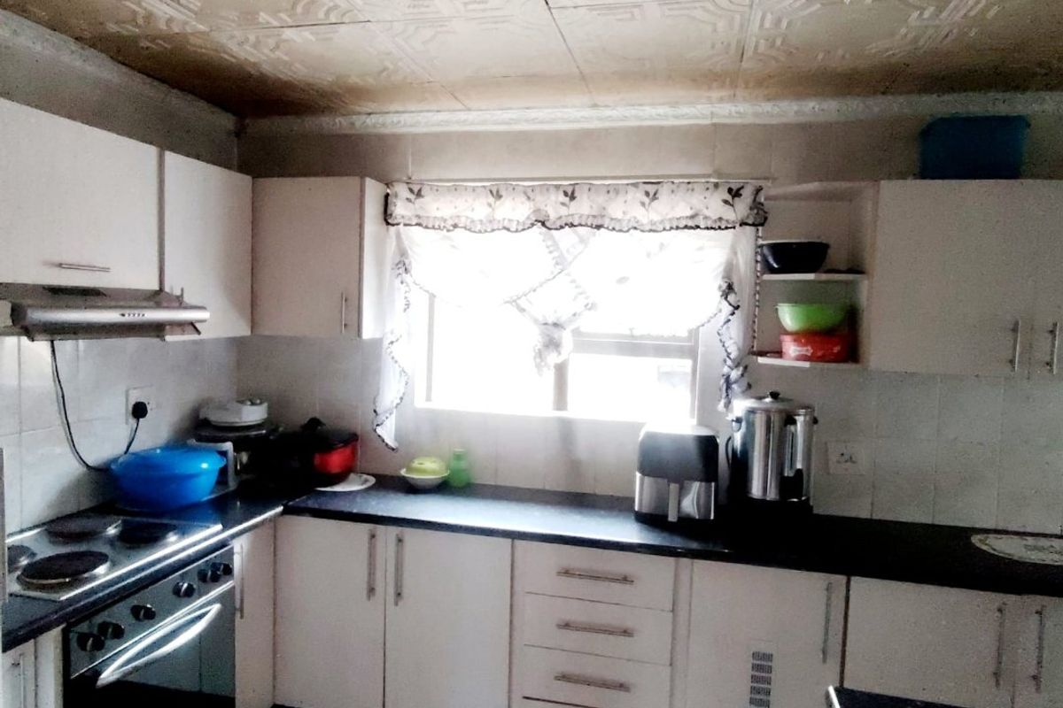 A functional kitchen featuring built-in cabinetry, an electric stove with extractor fan, tiled backsplash, and decorative ceiling tiles.