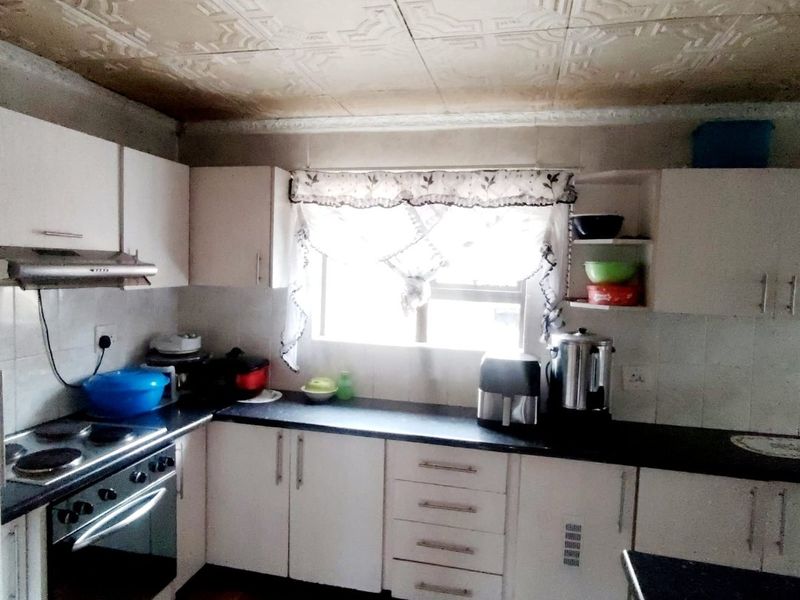 A functional kitchen featuring built-in cabinetry, an electric stove with extractor fan, tiled backsplash, and decorative ceiling tiles.