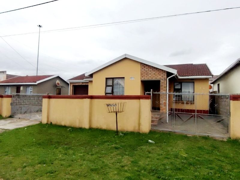 Front view of a single-story residential house featuring a perimeter wall, metal gate, and tiled roof in a suburban setting.