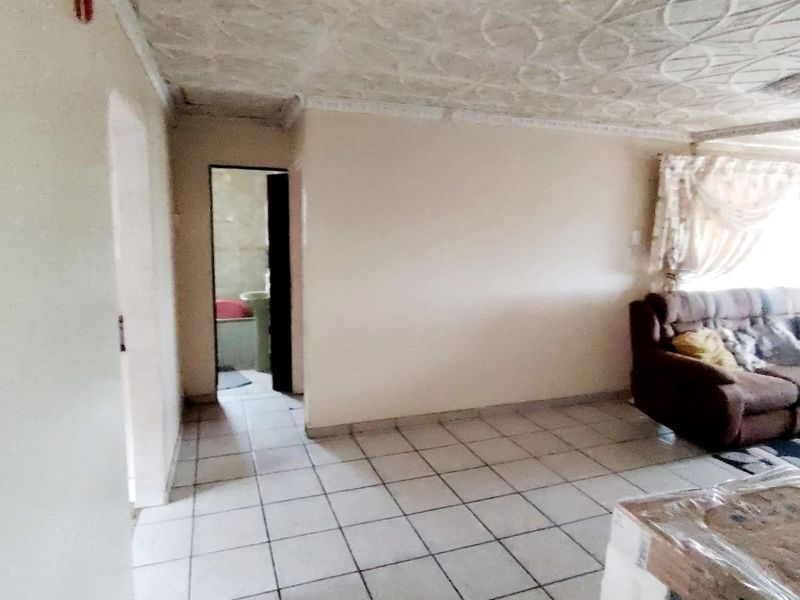 Living area featuring tiled flooring and a decorative ceiling, with an adjacent doorway leading to a bathroom.