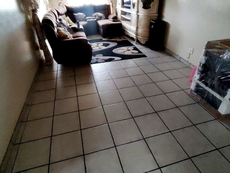 A living room area featuring ceramic tiled flooring and standard electrical fixtures, currently furnished with a large sectional sofa and media unit.