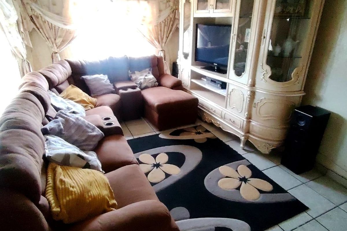 A living room featuring tiled flooring and a textured ceiling, currently furnished with a large sectional sofa and a built-in display cabinet.