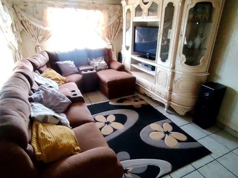 A living room featuring tiled flooring and a textured ceiling, currently furnished with a large sectional sofa and a built-in display cabinet.