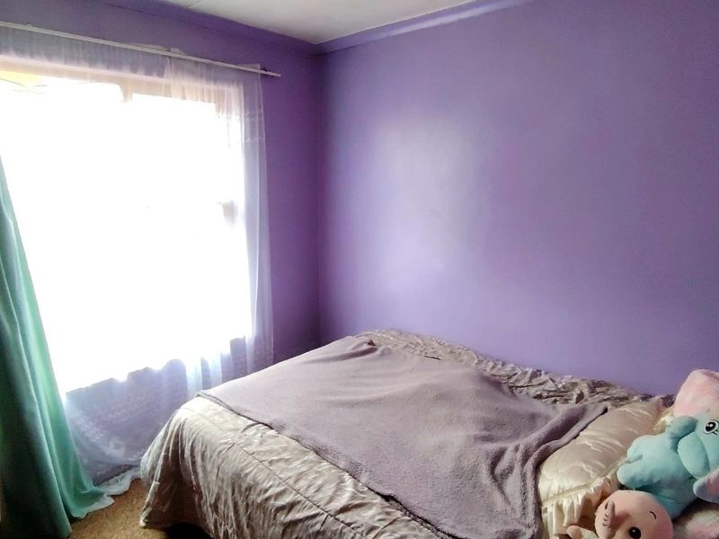 A bedroom featuring purple painted walls and carpet flooring, providing a functional space with natural light from the window.