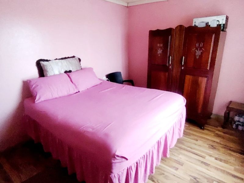 A bedroom featuring pink walls and wood-look flooring, requiring cosmetic updates to improve the overall aesthetic and finish.