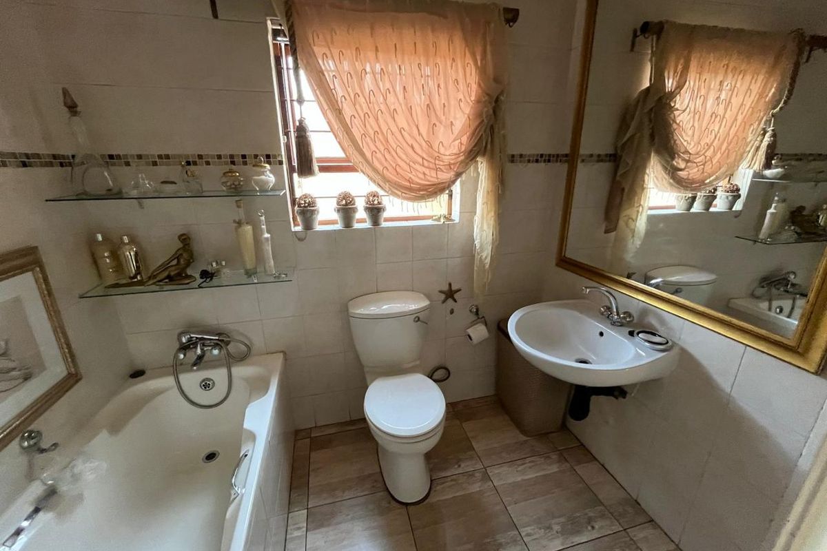 A functional bathroom featuring a built-in bathtub, wall-mounted basin, toilet, and tiled finishes, offering a classic layout with potential for modern updates.