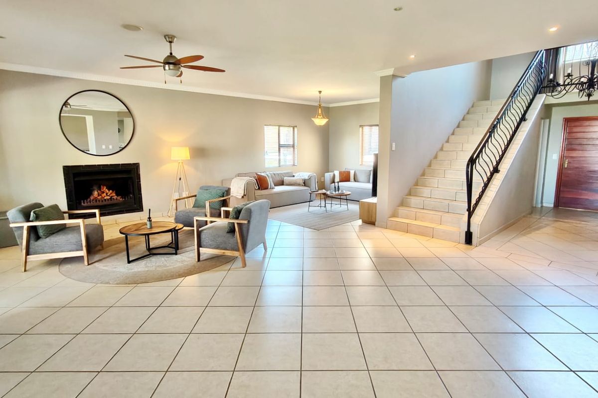 Spacious open-plan living area featuring tiled flooring, a built-in fireplace, and a grand staircase with a decorative wrought iron balustrade.