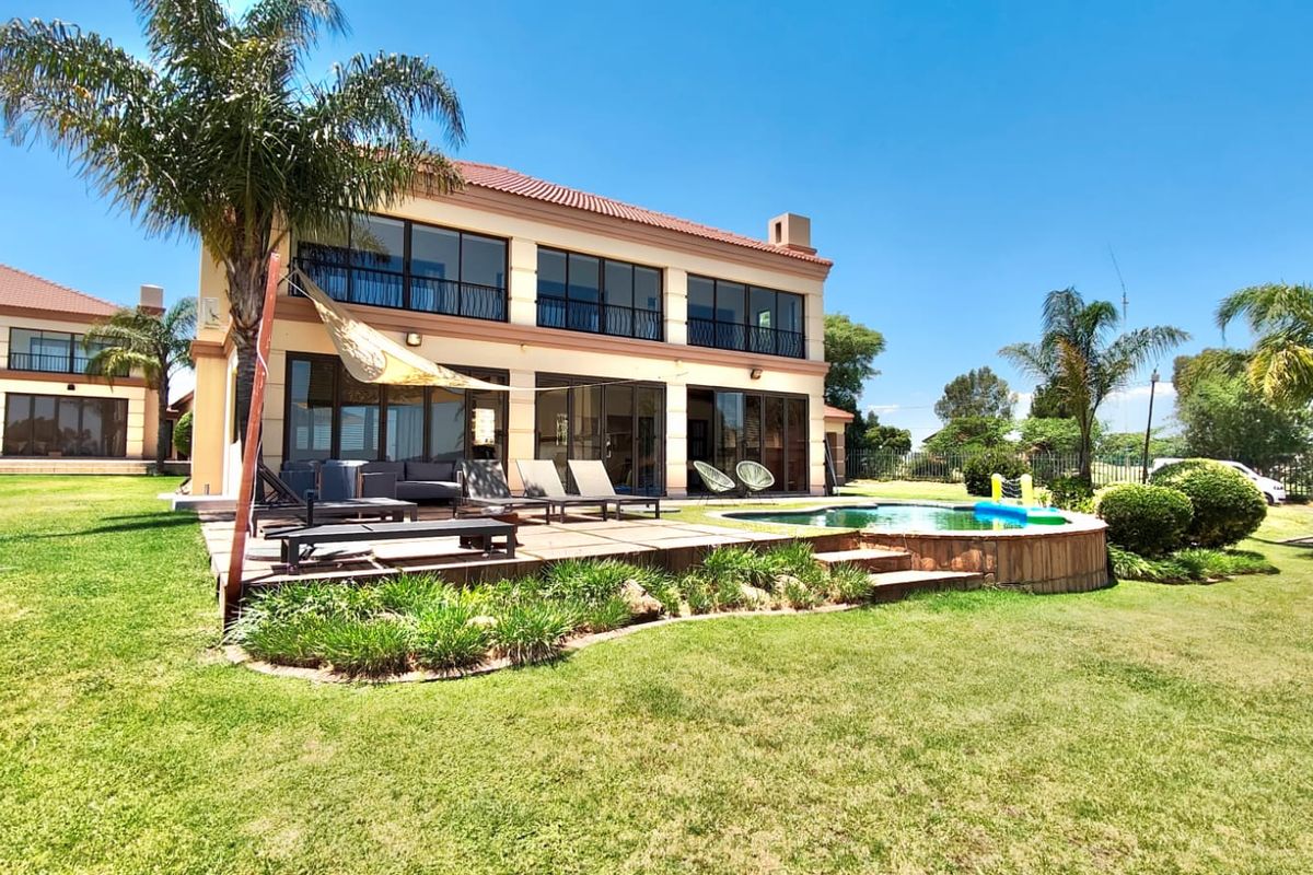 Rear view of a two-story house featuring a swimming pool, spacious tiled patio, and large sliding glass doors opening onto the landscaped garden.