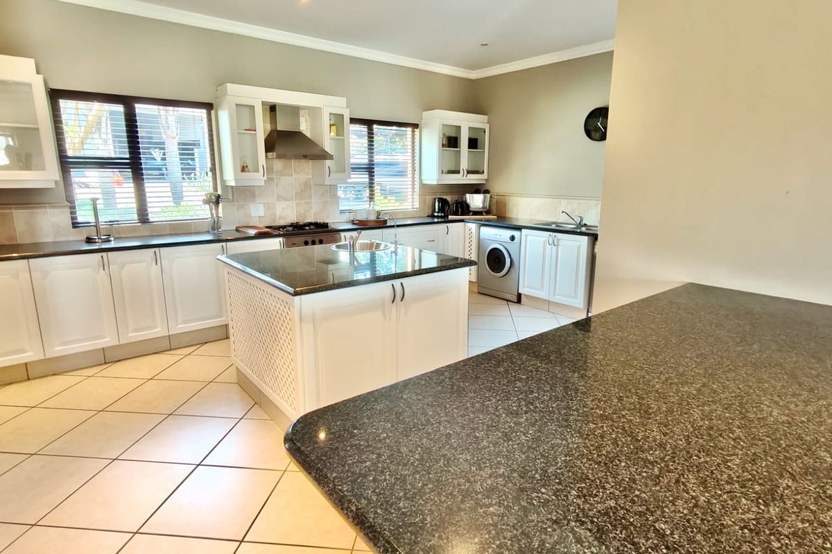 Spacious kitchen featuring a central island, granite countertops, ample built-in cabinetry, and integrated appliances, finished with neutral tiled flooring.
