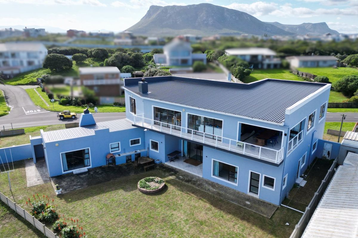Aerial view of a two-story blue house featuring a metal roof, upper-level balcony, and a rear garden area with mountain views.