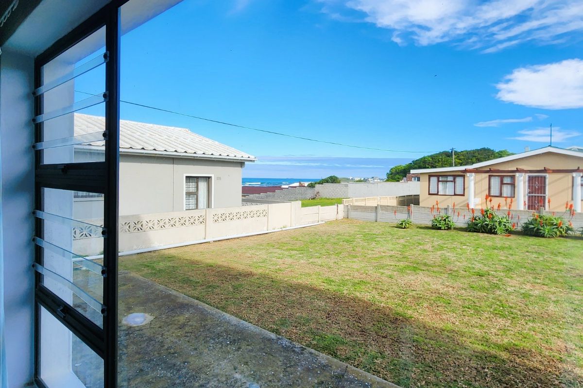A view of the rear garden featuring a concrete patio, lawn, and perimeter wall, with a distant ocean view.