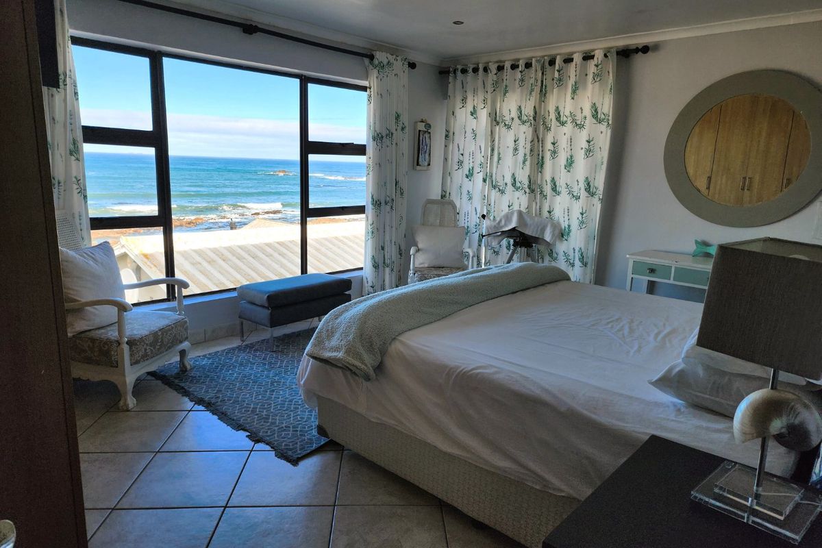 A bright bedroom featuring large windows with expansive ocean views, tiled flooring, and recessed ceiling lighting.