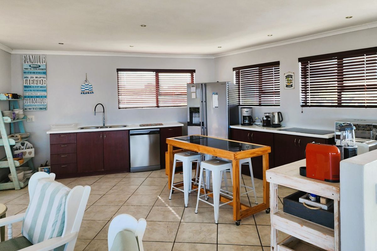 A functional kitchen featuring dark wood cabinetry, tiled flooring, integrated dishwasher, and ample natural light through multiple windows with venetian blinds.