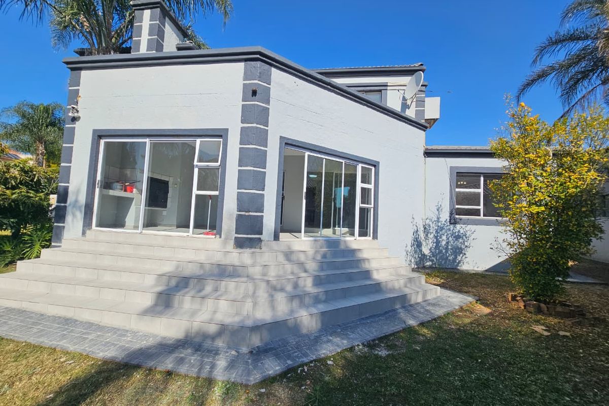 Rear view of the house featuring a raised tiled patio area with sliding glass doors and a paved garden walkway.