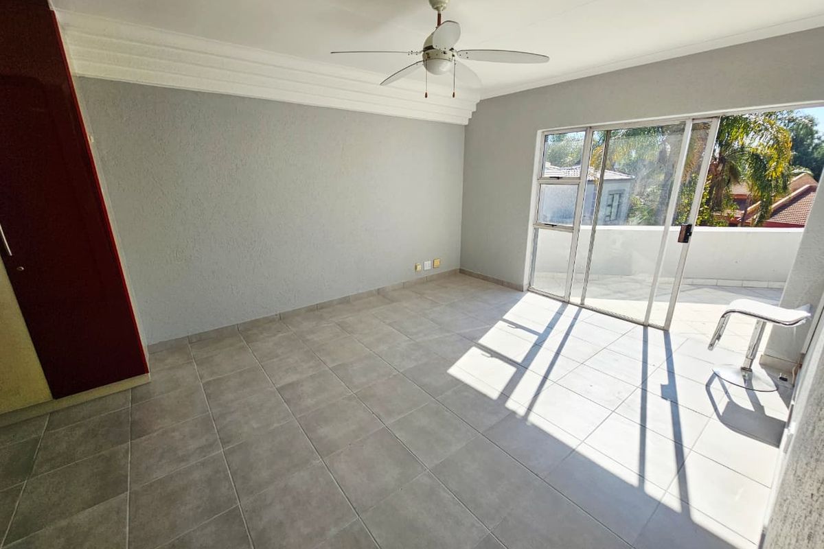 A bright, empty bedroom featuring tiled flooring, a ceiling fan, built-in cupboards, and a sliding glass door leading to an outdoor balcony.