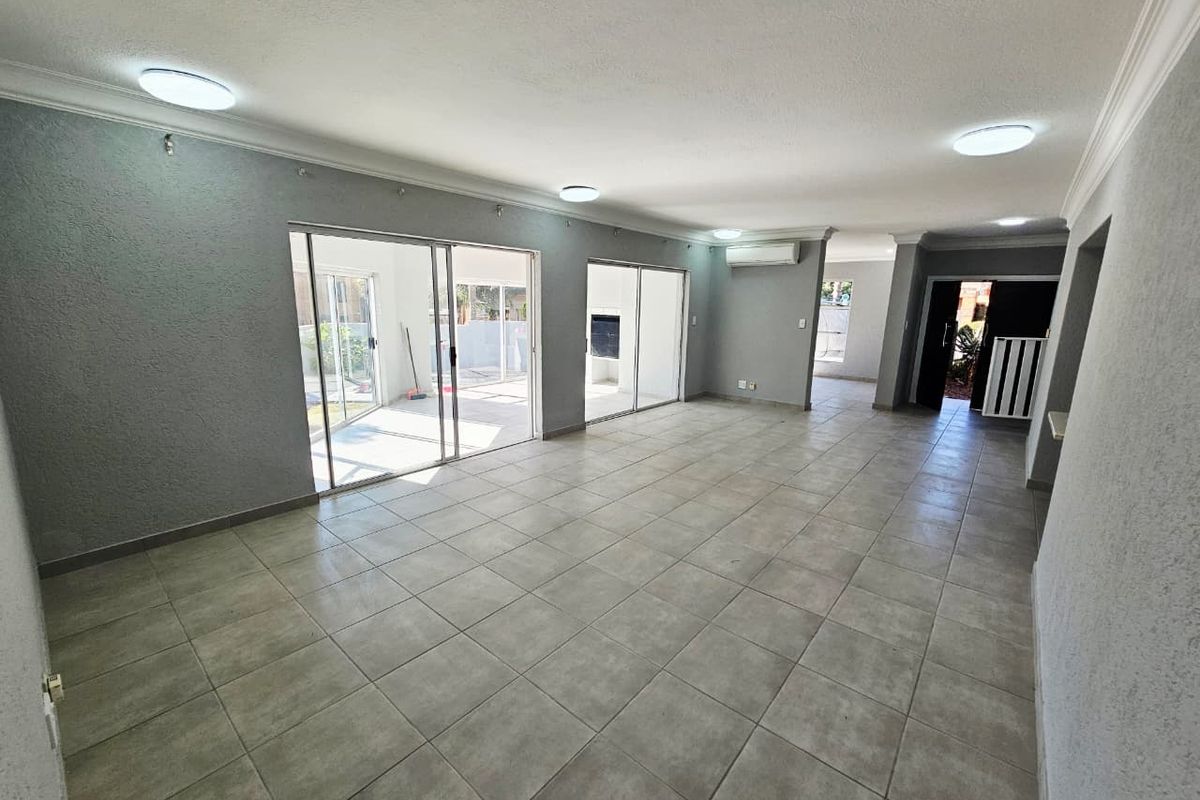 Spacious, open-plan living area featuring neutral tiled flooring, modern recessed lighting, and large sliding glass doors providing seamless access to the outdoor patio.
