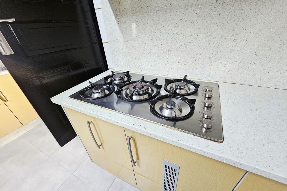 A kitchen workspace featuring a built-in gas hob set into a stone countertop with light-toned cabinetry and a ventilation grille.