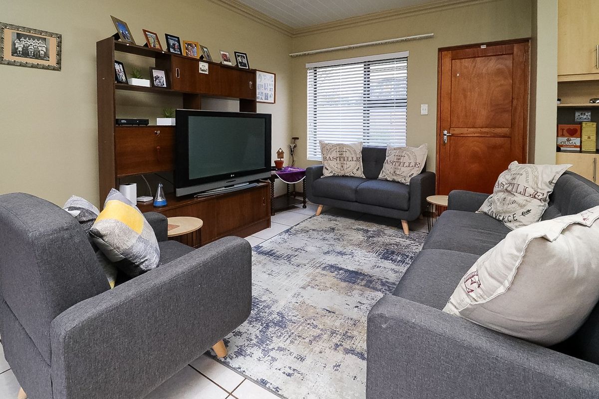 A comfortable living room featuring tiled flooring, a coved ceiling, and natural light through venetian blinds.