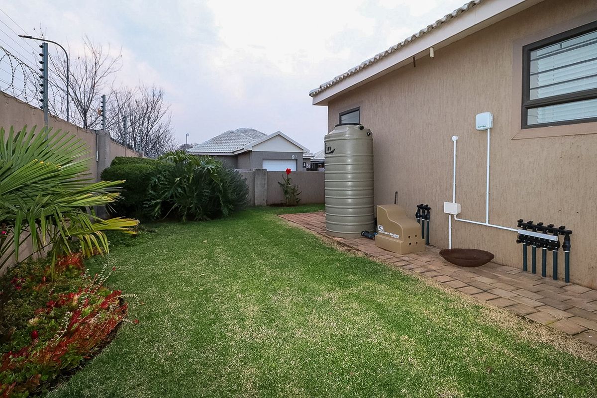 A well-maintained rear garden featuring a paved walkway, water storage tank, and integrated irrigation system, enclosed by a secure boundary wall with electric fencing.