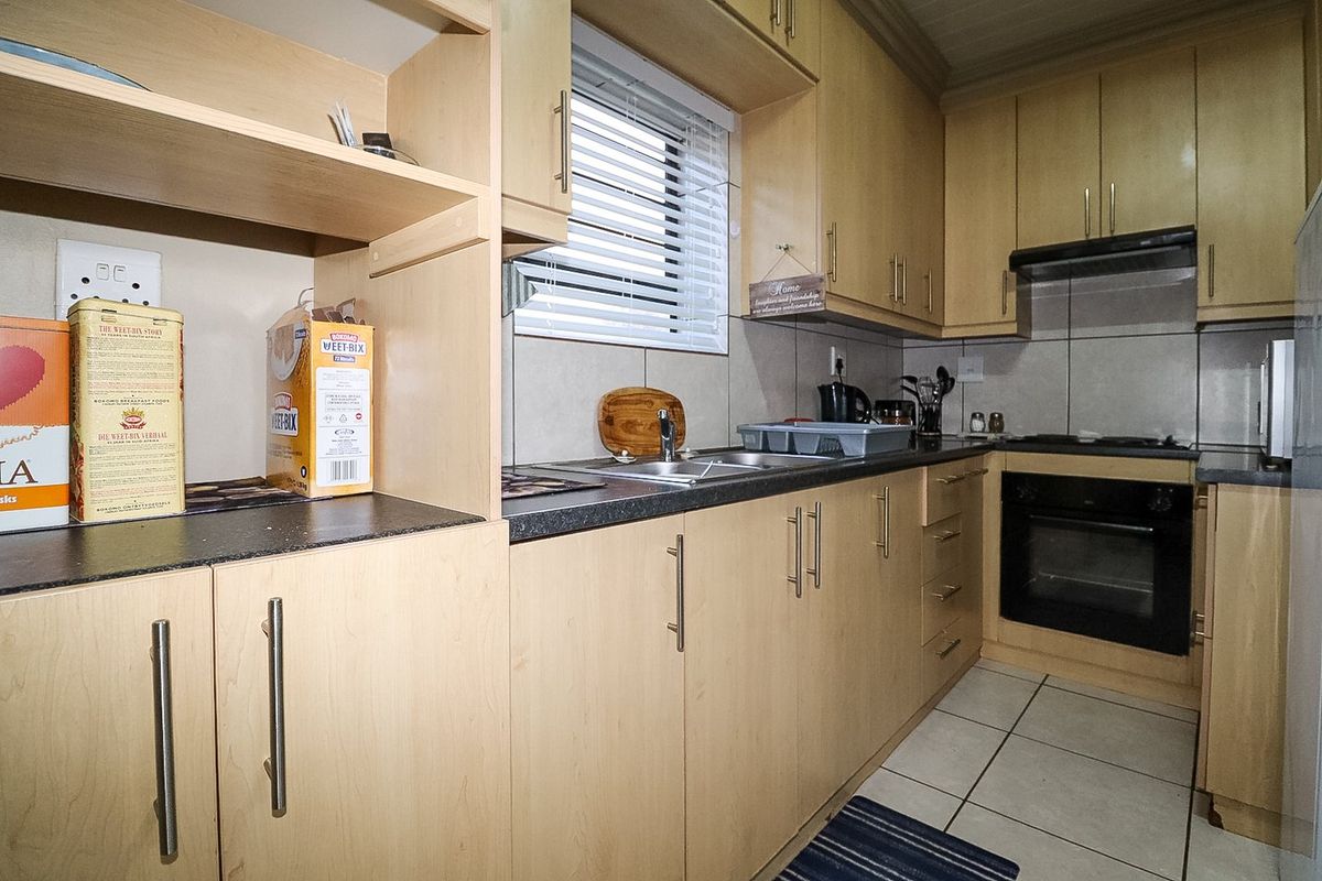 A functional kitchen featuring light wood laminate cabinetry, granite countertops, built-in oven, hob, extractor fan, and tiled flooring.