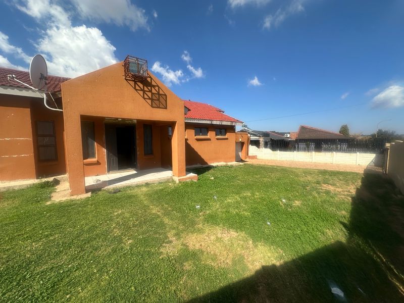Rear view of the house featuring a terracotta tiled roof, orange exterior walls, and a spacious backyard with a concrete boundary wall.