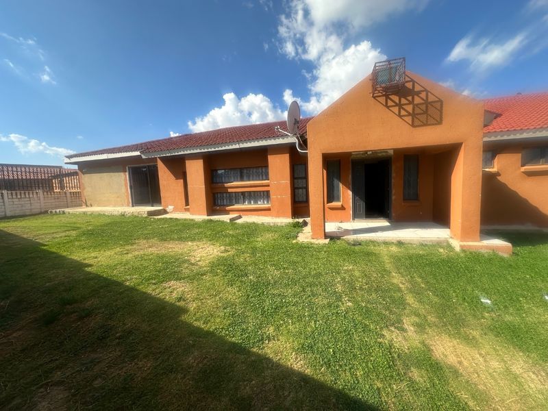 Rear view of a single-story house featuring a tiled roof, security bars on windows, and a small concrete patio area overlooking the lawn.