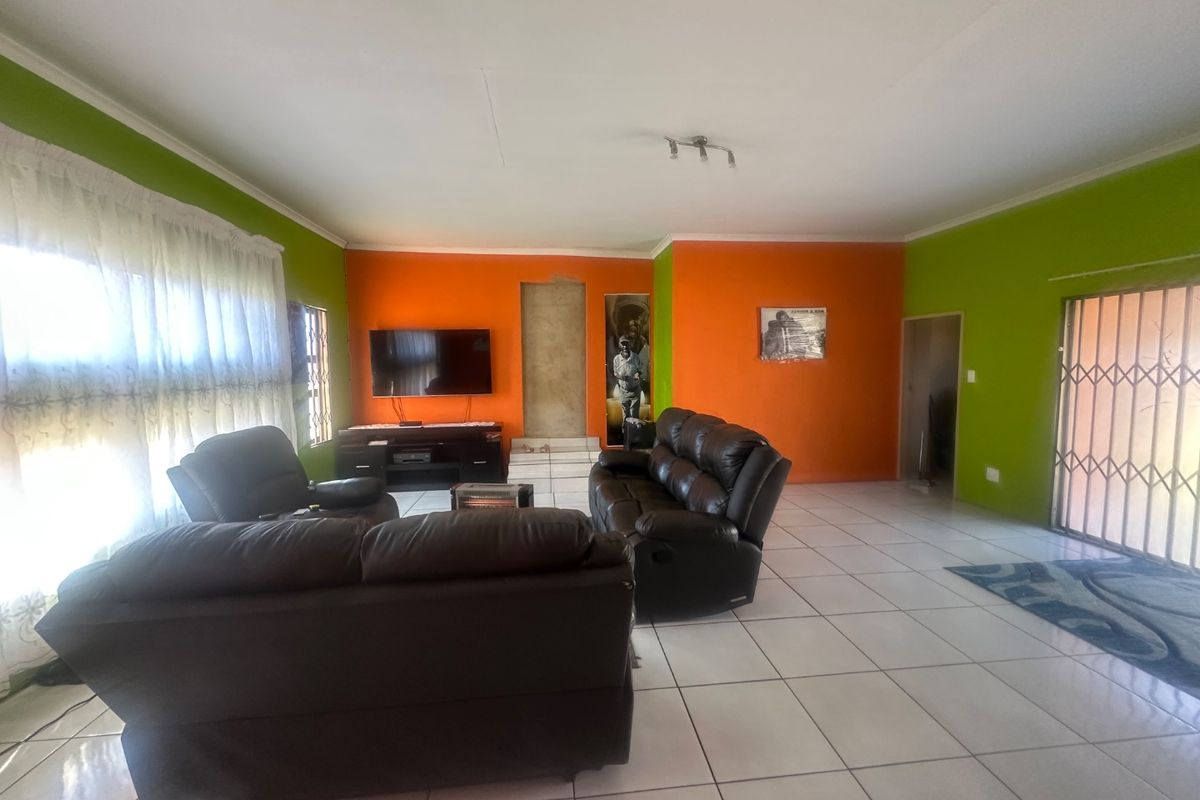 Spacious living room featuring ceramic floor tiles, bright accent walls, and a security gate leading to the exterior.