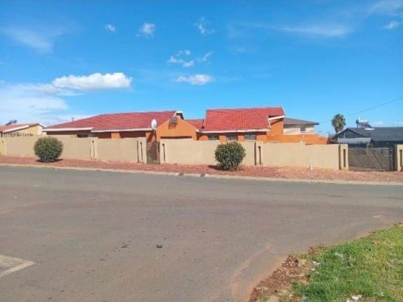 A street-level view of the property featuring a perimeter wall, tiled roof, and gated entrance.