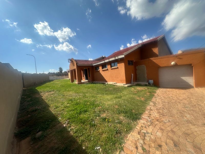 Front exterior view of a single-story house featuring a tiled roof, attached garage, paved driveway, and a surrounding boundary wall.