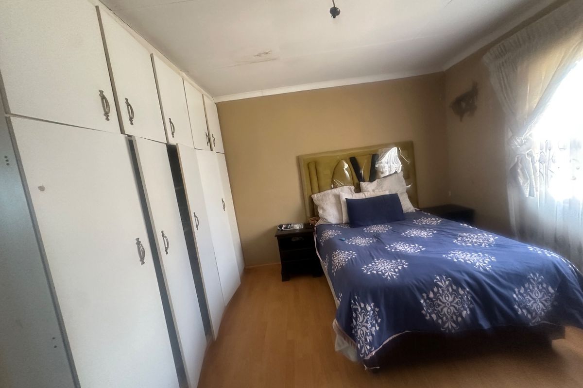 Bedroom featuring built-in cupboards and laminate flooring. The room shows signs of ceiling and wall wear, offering potential for cosmetic updates.