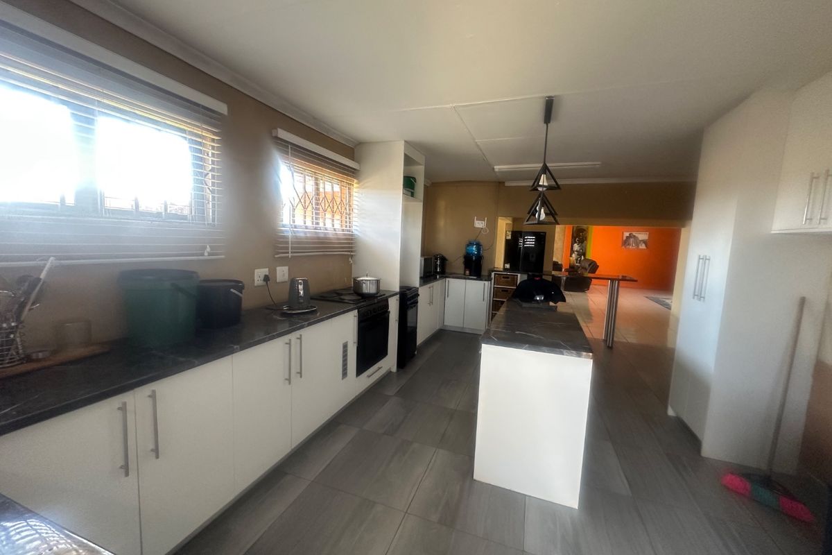 A functional kitchen featuring white cabinetry, a central island, dark countertops, and tiled flooring, with an open-plan layout leading to the living area.