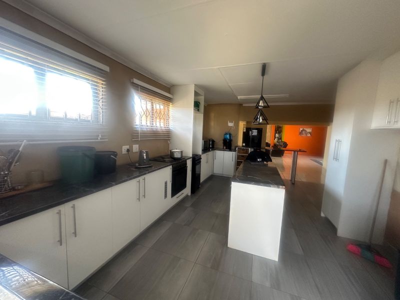 A functional kitchen featuring white cabinetry, a central island, dark countertops, and tiled flooring, with an open-plan layout leading to the living area.