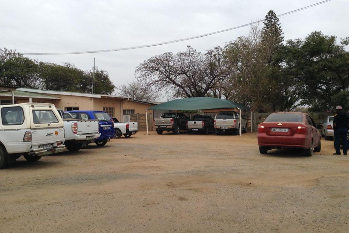 Exterior view of the property frontage featuring an unpaved parking area and a covered carport structure.