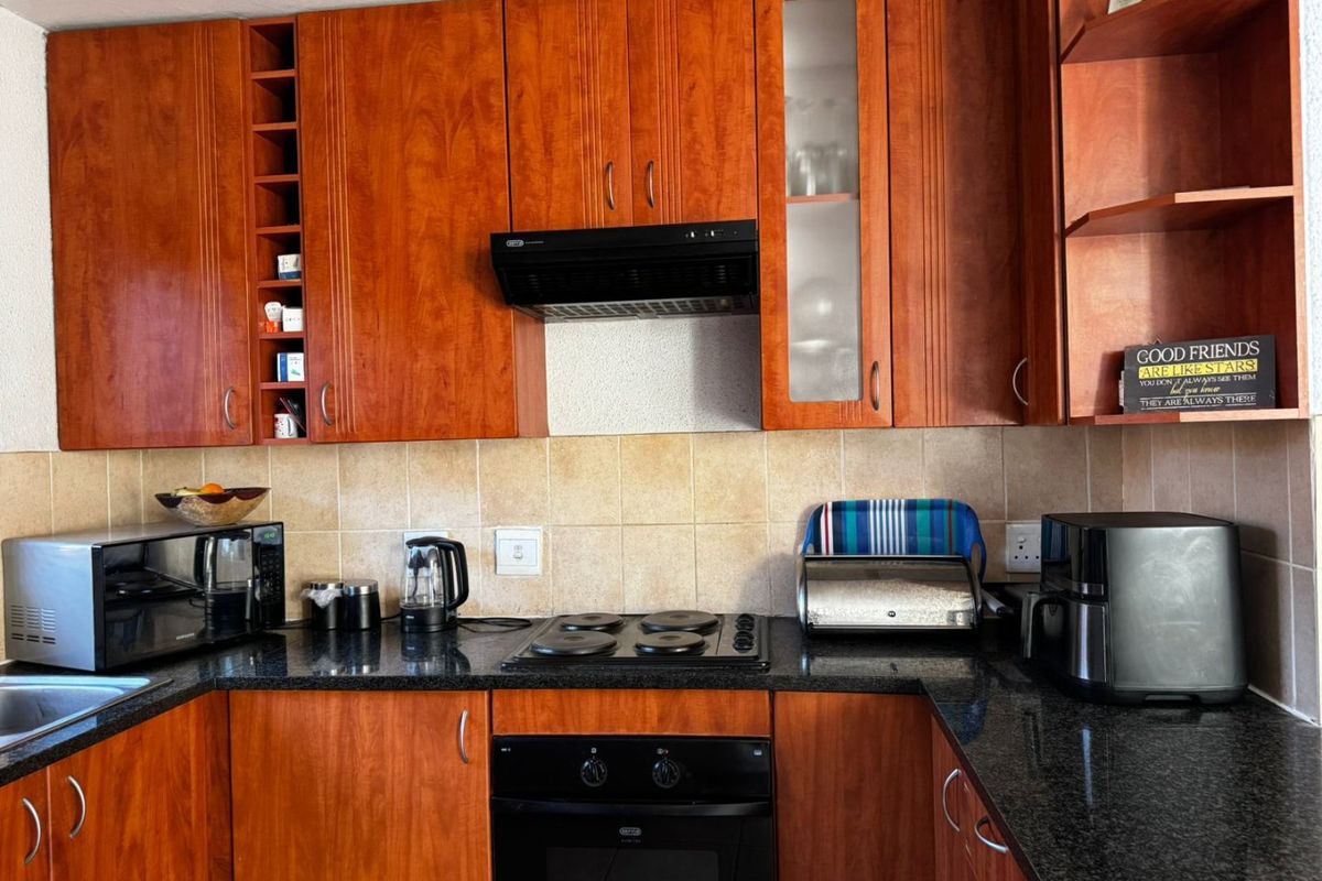 A functional kitchen featuring warm-toned wooden cabinetry, dark granite countertops, a built-in oven, electric hob, and a tiled backsplash.