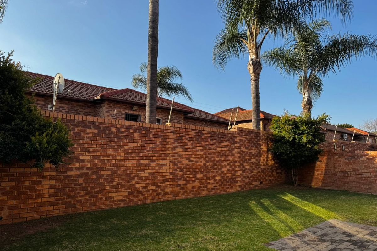 A private rear garden featuring a well-maintained lawn, paved section, and high brick boundary walls with mature palm trees.