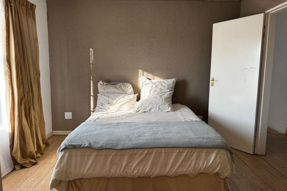A bedroom featuring tiled flooring and a textured brown feature wall, providing a neutral base for interior design updates.