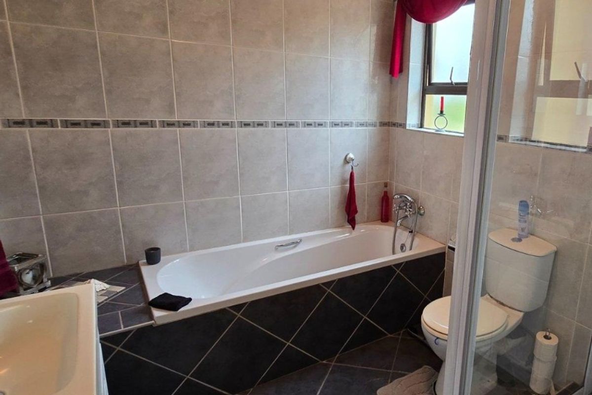 A functional bathroom featuring a built-in bathtub, a separate shower enclosure, and a toilet, finished with neutral wall tiles and dark floor tiles.