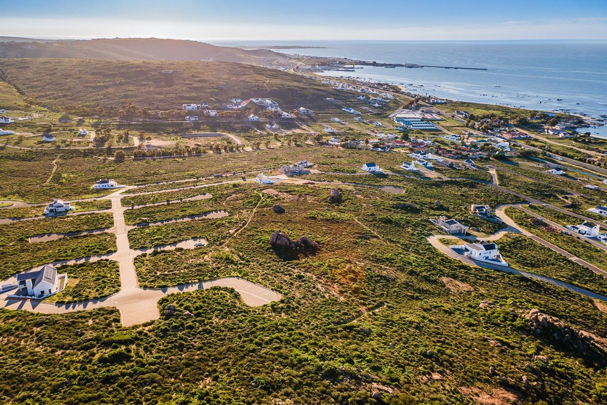 An aerial view of a coastal residential development featuring paved roads and established plots set within a natural landscape.