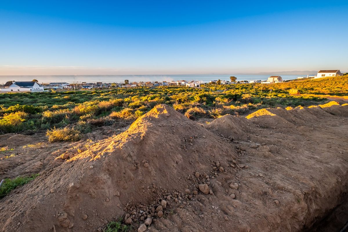 A scenic view overlooking a coastal residential area with natural vegetation and earth mounds in the foreground.