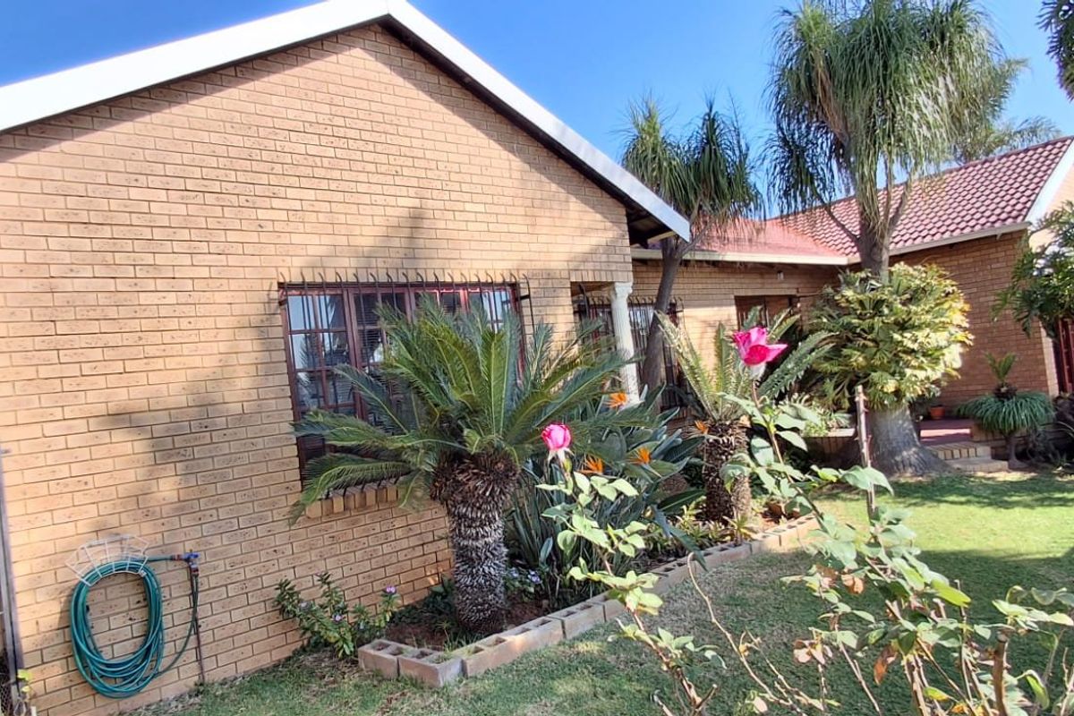 A view of the rear face brick facade of the house, featuring a well-maintained garden and established landscaping.