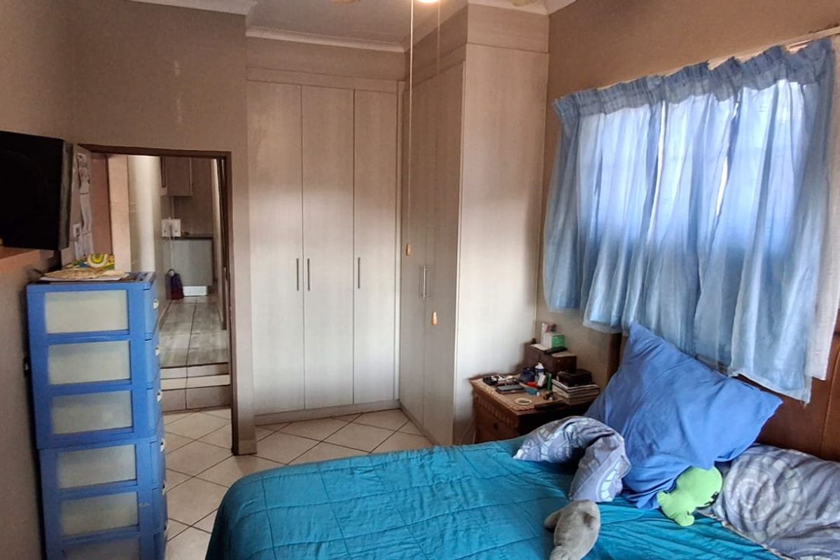 A functional bedroom featuring built-in cupboards, tiled flooring, and a ceiling fan, providing a practical living space.