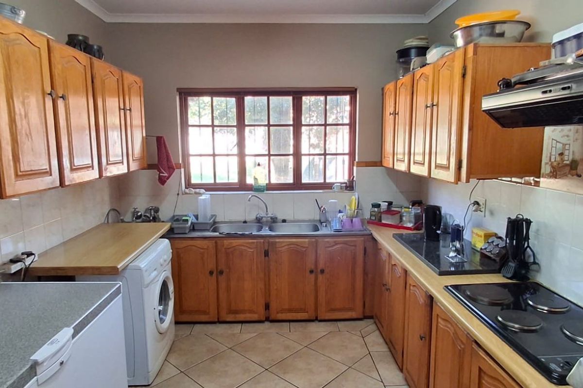 A functional kitchen featuring wooden cabinetry, tiled splashbacks, a double basin sink, and a built-in electric hob with an extractor fan.
