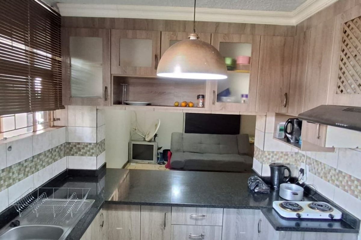 A functional kitchen featuring laminate cabinetry, granite countertops, tiled backsplash, and an integrated extractor fan, with a pass-through window to the living area.