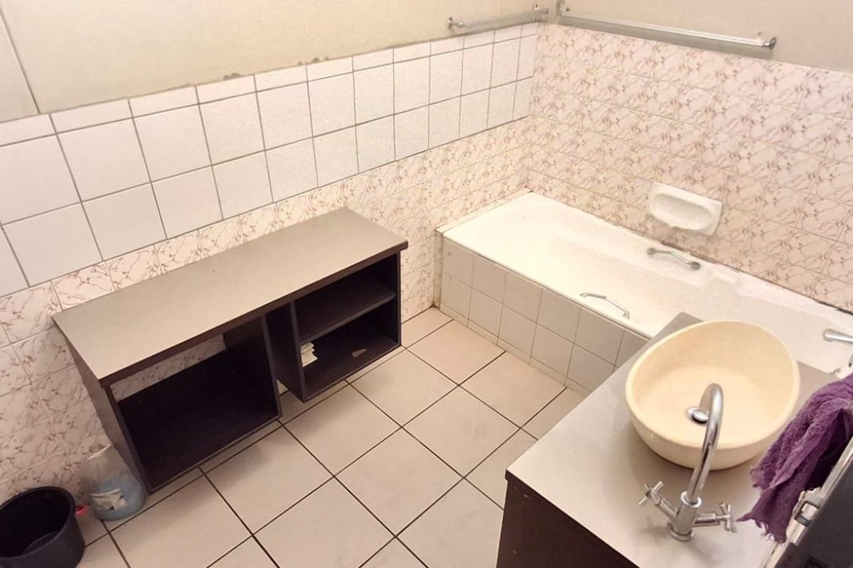 A dated bathroom featuring a built-in bathtub, vessel sink, and tiled finishes, requiring cosmetic updates to modernize the space.
