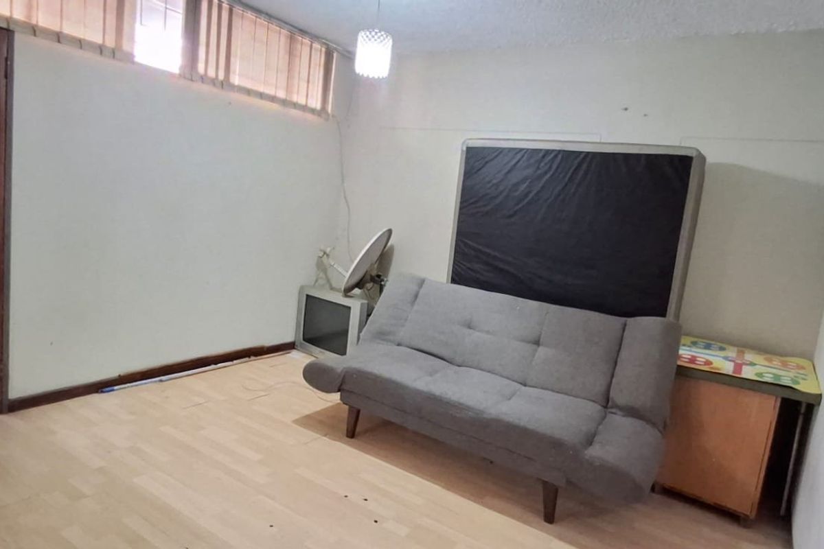 A living room featuring laminate flooring, textured ceilings, and high-level clerestory windows, requiring cosmetic updates to improve its overall condition.