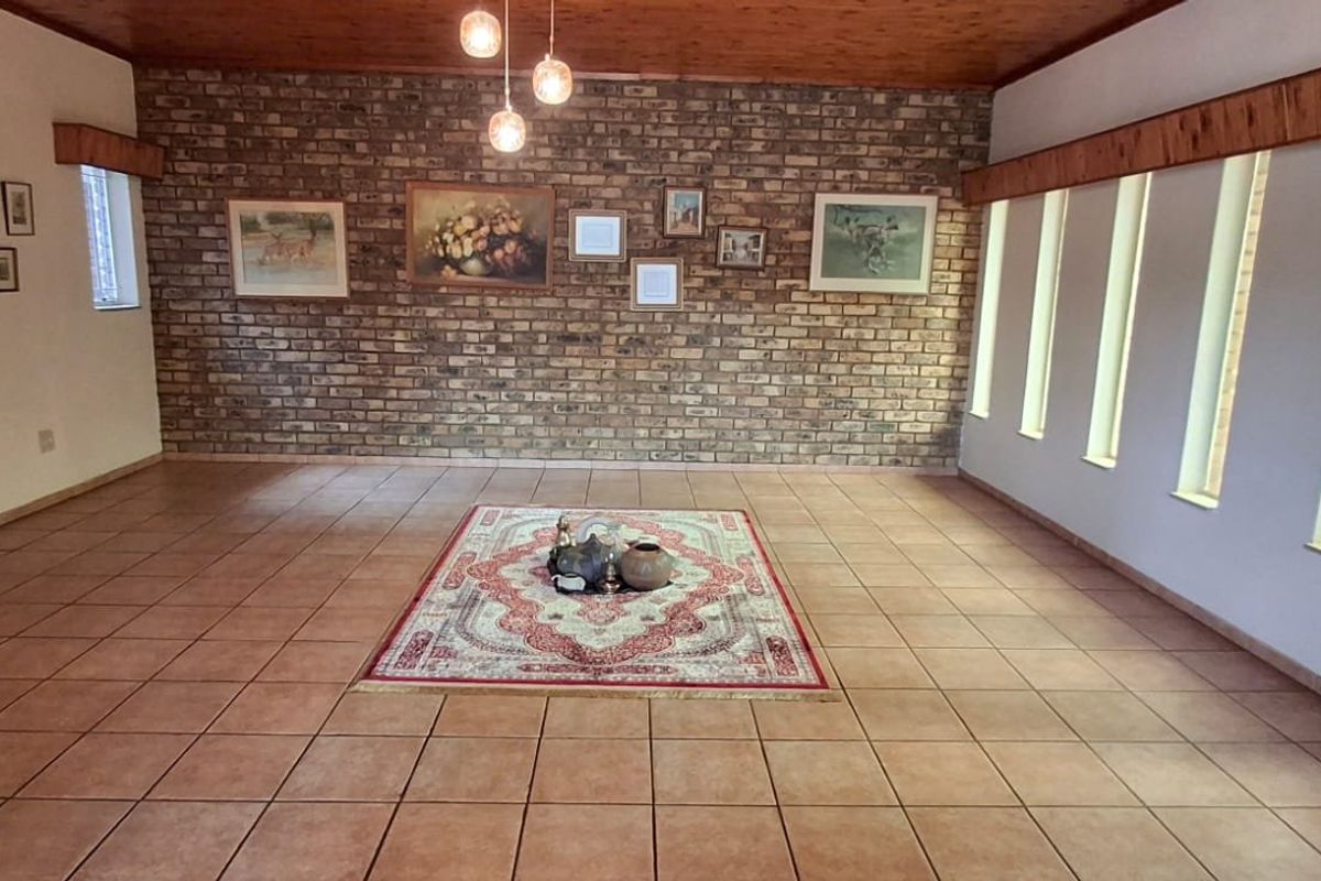 Spacious living area featuring an exposed brick feature wall, timber ceiling, and ceramic tiled flooring with natural light from vertical windows.