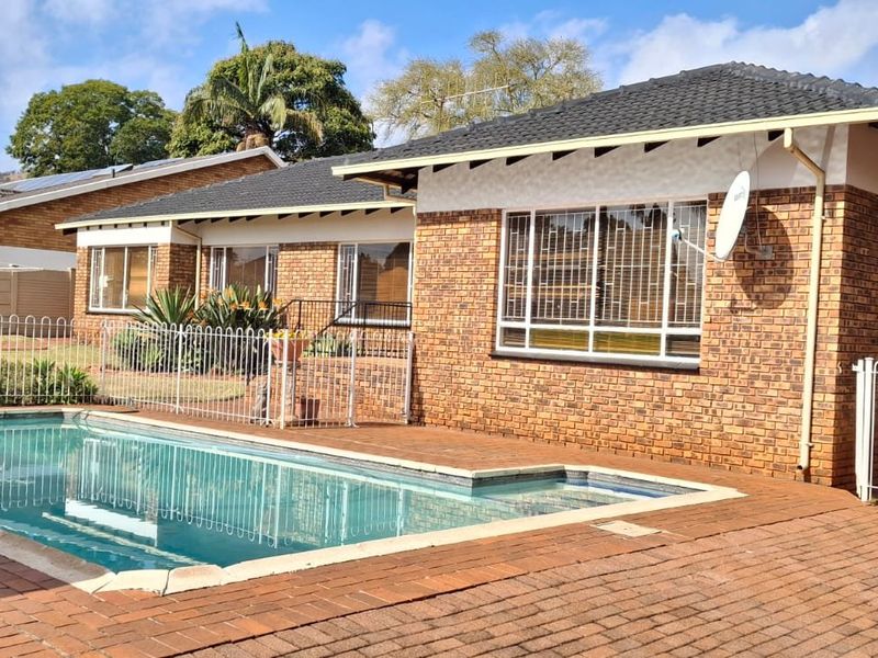 Rear exterior view of a face brick house featuring a swimming pool, paved patio area, and secure metal fencing.