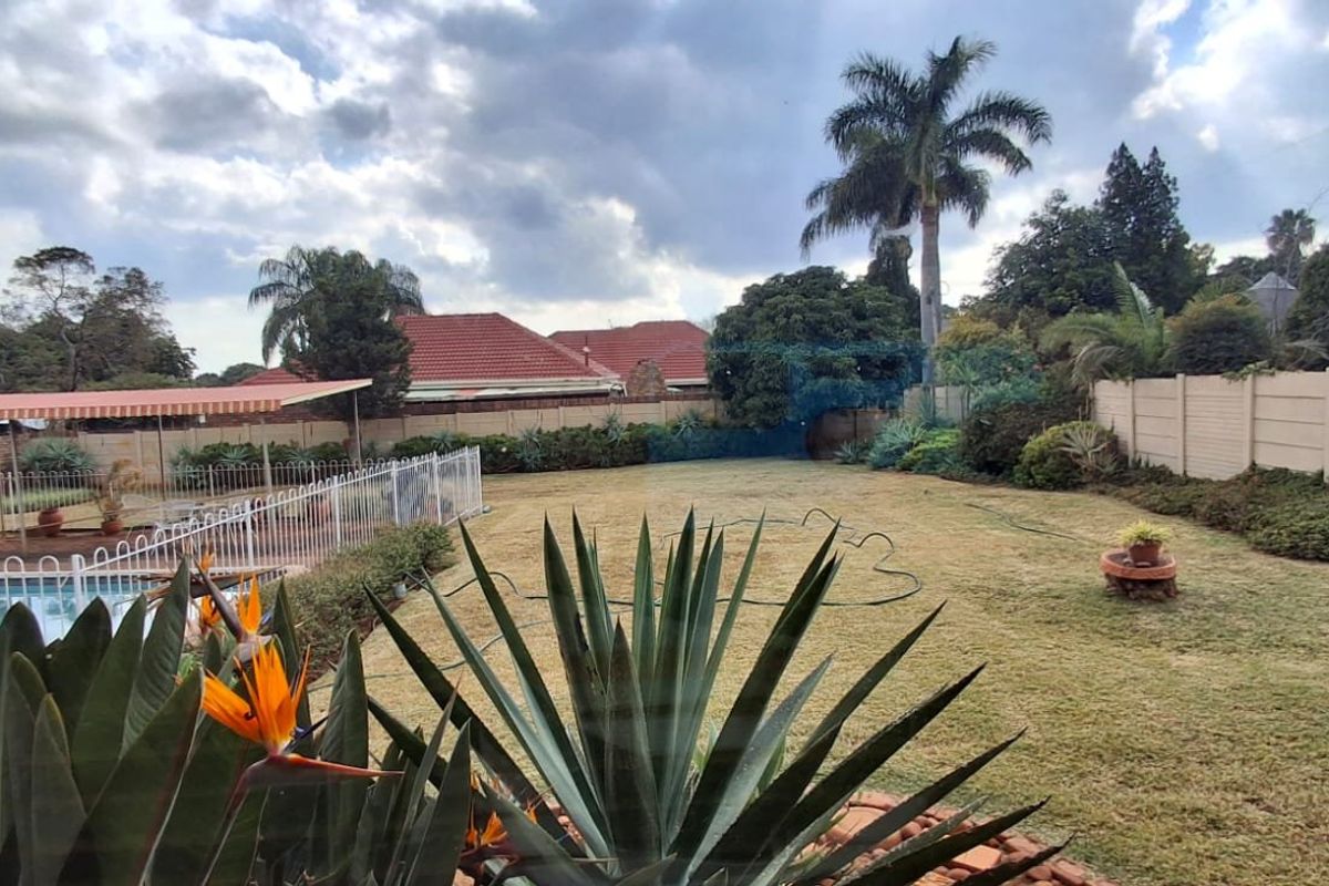 Spacious rear garden featuring a swimming pool with safety fencing, a covered patio area, and established perimeter boundary walls.