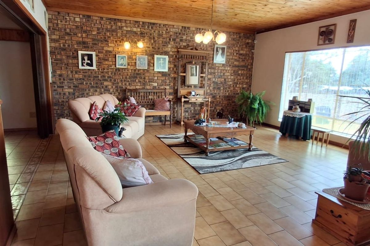 Spacious living room featuring an exposed brick feature wall, timber ceiling, and ceramic floor tiles with large windows providing natural light.
